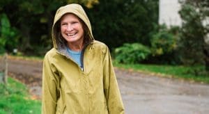 Julie Wolcott shown outside in raincoat with hood up, smiling. 